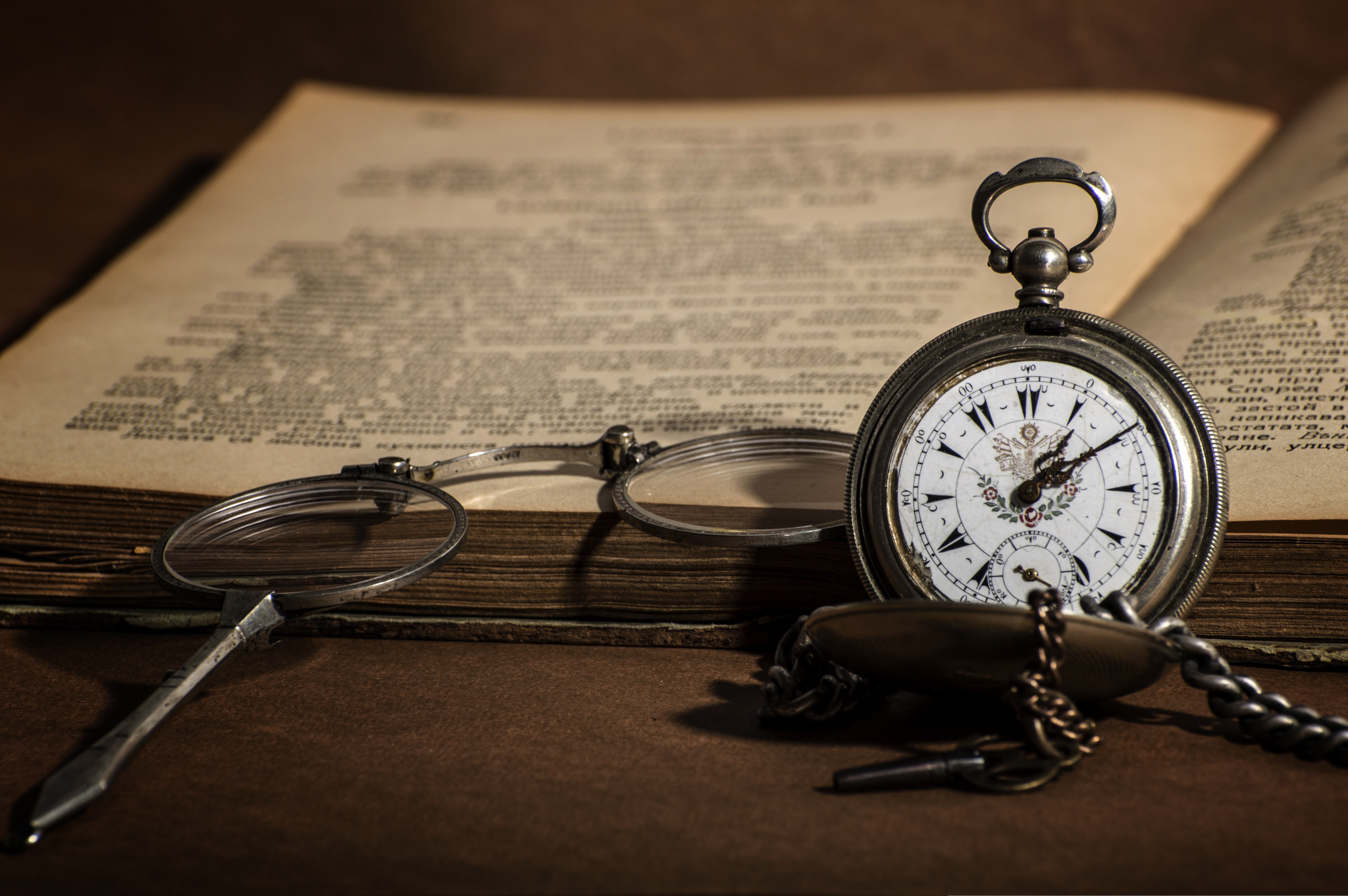 An older book with glasses and a stopwatch nect to it
